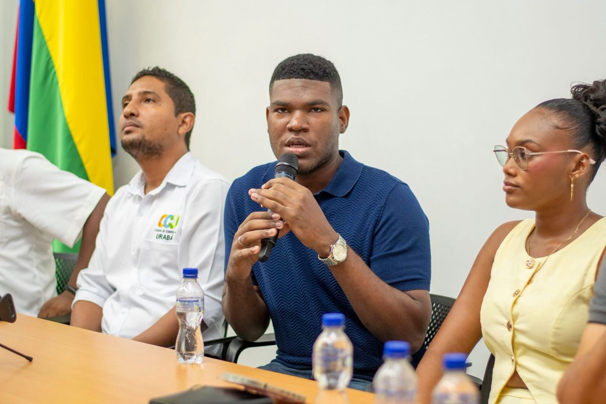 Joven expone con micrófono en un panel junto a otros participantes